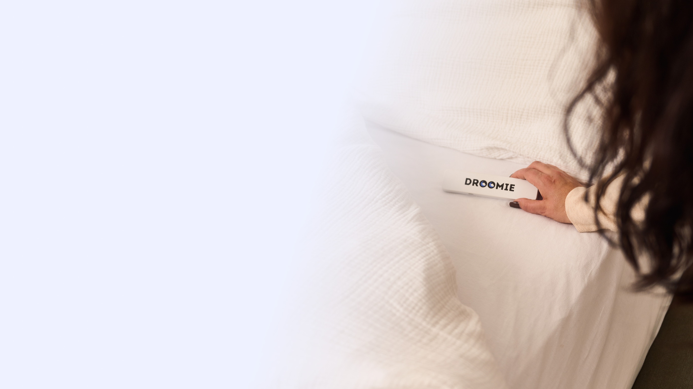 Hand die een Droomie slaaphulp apparaat bedient op een wit bed voor een betere nachtrust.
